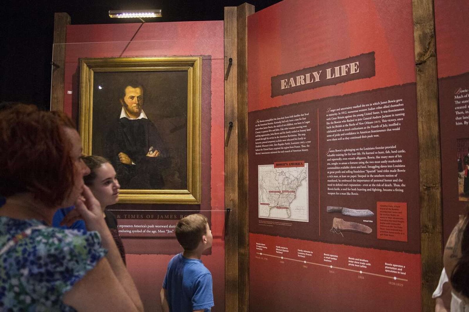 Visitors reading the Early Life panel beside a framed portrait of Jim Bowie in the exhibit gallery.