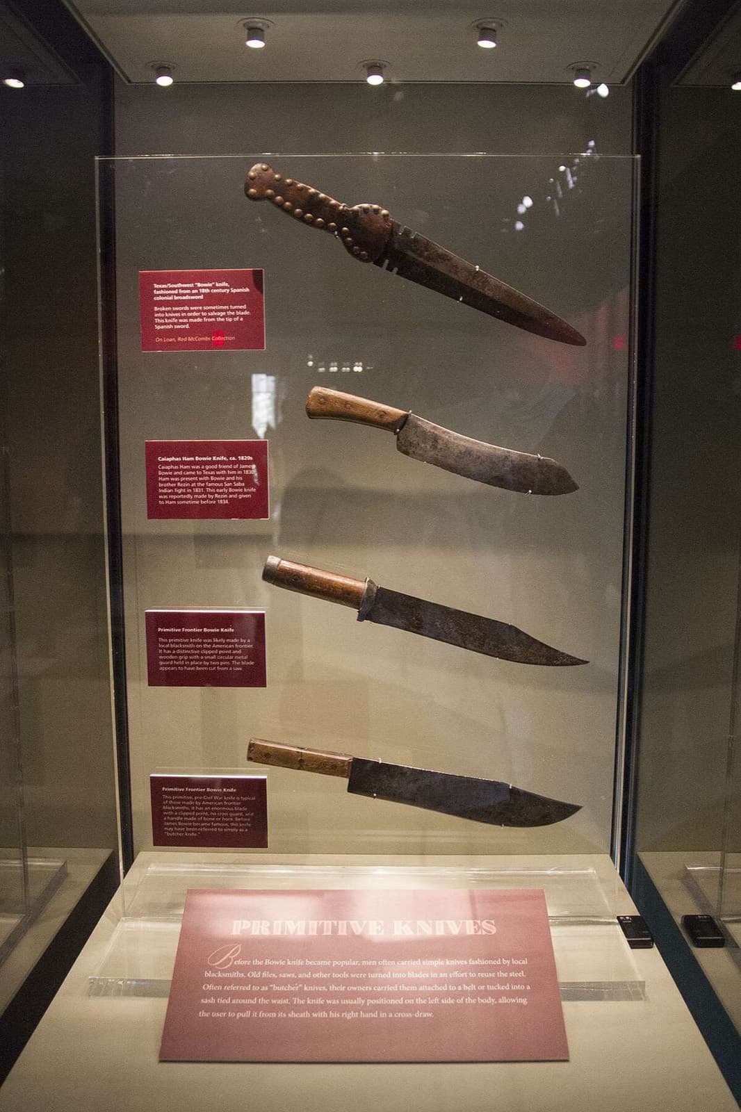 A lit display case holding four early knives, each with its own descriptive label.